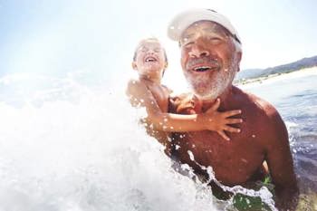 An older man and a young child laughing in the surf